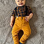 baby, child, smiling, plaid_shirt, suspenders, mustard_pants, blue_socks, lying_down, fluffy_rug, soft_texture, happy, cute, infant, casual_clothing, indoors, portrait, one_person, toddler, clothing, fashion