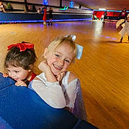 Kadason is registered to the contest to win money with this photo: child, children, smiling, bow, roller_skating, skating_rink, blue_barrier, indoor, floor, lights, people, fun, playful, happy, girl, costume, event, activity, leisure, young