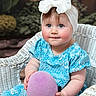 baby, child, blue_dress, headband, bow, wicker_chair, purple_ball, rosy_cheeks, blue_eyes, outdoor, greenery, portrait, cute, sitting, soft_toy, infant, smile, playful, young_child, natural_light