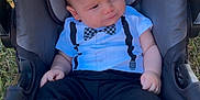 Ahmed Adam is registered to the contest to win money with this photo: baby, infant, car_seat, outdoor, grass, clothing, black_pants, bow_tie, onesie, shoes, footwear, person, young_child, cute, portrait, sitting, sunlight, expression, head, face