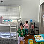 child, children, bunk_bed, bedroom, toy_kitchen, activity_table, carpet, window_blinds, wooden_floor, clothing, hair_beads, play, indoor, furniture, person, room, white_wall, sneakers, pajamas, ladder