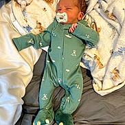 Kacen joined the competition — help win amazing prizes! baby, newborn, infant, pacifier, onesie, green_clothing, dinosaur_feet, blanket, bed, sleeping, face, person, cute, soft_texture, indoor, cozy, footwear, paw_prints, infant_clothing, resting