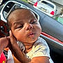 baby, infant, child, person, car_interior, dashboard, hand, skin, clothing, white_shirt, face, expression, seat, vehicle, window, daylight, portrait, cute, young, holding