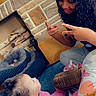 child, baby, infant, portrait, curly_hair, smiling, pink_pajamas, sitting, lying_down, fireplace, brick_wall, plush_toy, rainbow_toy, indoor, home, carpet, basket, wood, family, candid