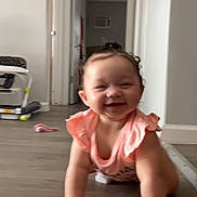 Alani is registered to the contest to win money with this photo: baby, child, infant, crawling, smiling, happy, portrait, indoor, home, hallway, floor, toy, pink_outfit, ruffles, curly_hair, face, hands, arms, video_call, smartphone_screenshot