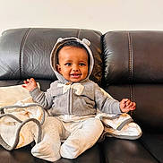 Alex joined the competition — help win amazing prizes! baby, child, smile, hoodie, gray_clothing, blanket, couch, leather_furniture, sitting, happy, infant, indoor, cute, portrait, warm, cozy, hands, feet, headwear, comfortable