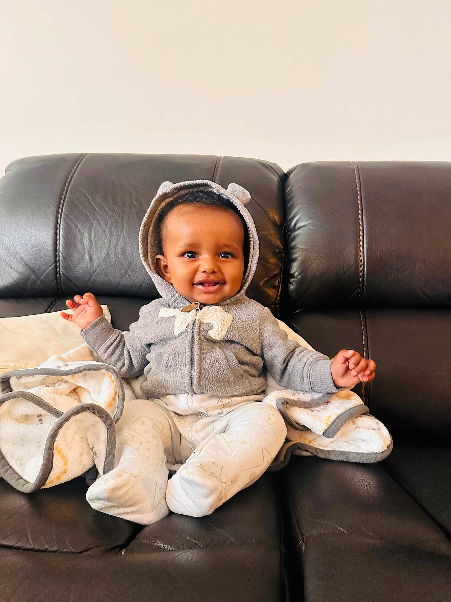 Alex joined the competition — help win amazing prizes! baby, child, smile, hoodie, gray_clothing, blanket, couch, leather_furniture, sitting, happy, infant, indoor, cute, portrait, warm, cozy, hands, feet, headwear, comfortable