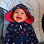 baby, cheerful, child, clothing, couch, cute, face, floral_pattern, happy, hoodie, indoor, infant, navy_blue, person, pillow, pink, portrait, seated, smiling, young