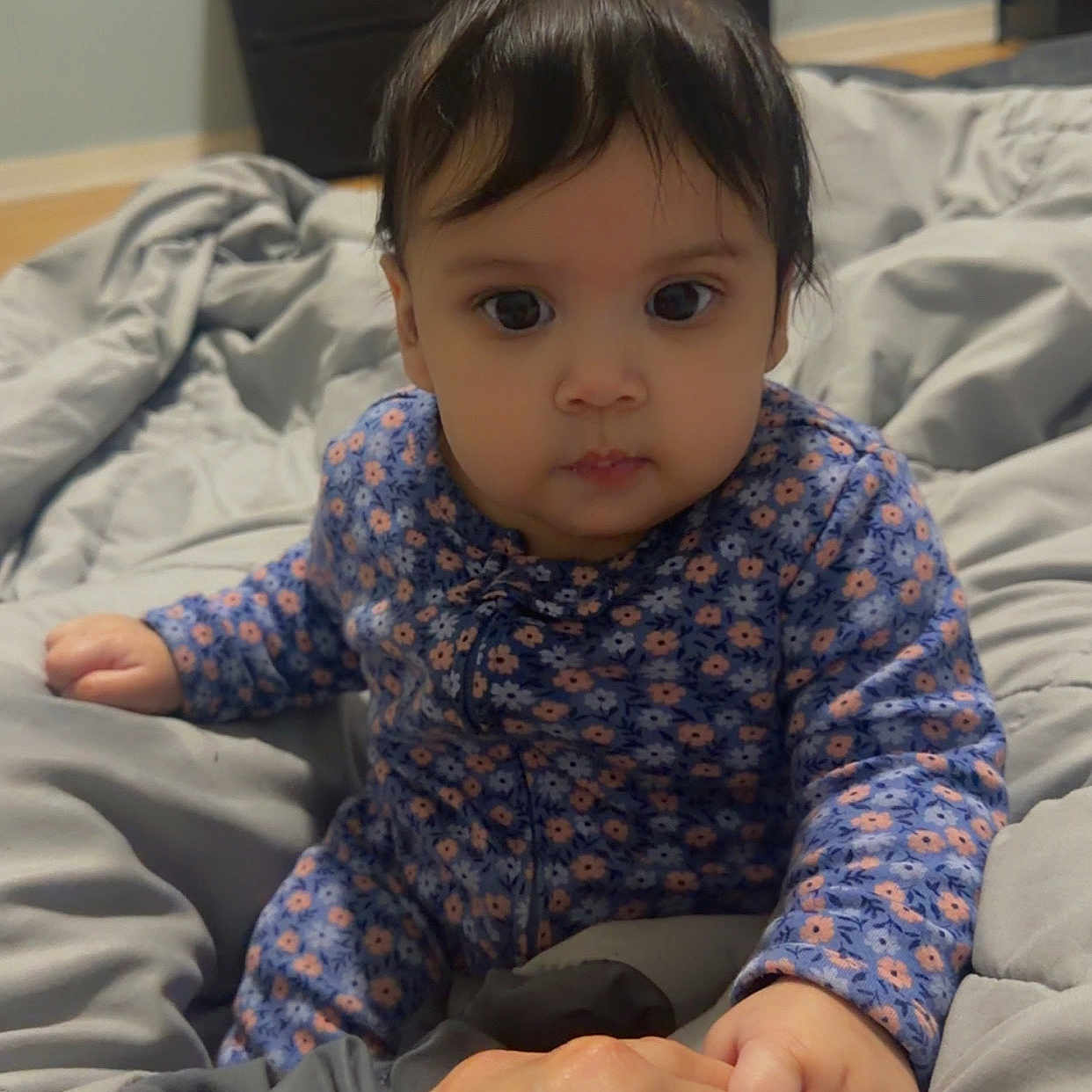 Jadeliz Linette is registered to the contest to win money with this photo: baby, child, onesie, blue_clothing, floral_pattern, hand, adult_hand, bed, blanket, gray_blanket, furniture, dresser, plush_toy, indoor, portrait, cute, person, infant, baby_grip, soft_lighting