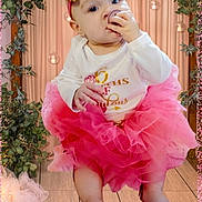 Laylani joined the competition — help win amazing prizes! baby, infant, child, pacifier, headband, bow, pink_tutu, tutu, onesie, barefoot, curtain, indoor, wooden_floor, hanging_lights, greenery, party_decor, celebration, portrait, cute, sitting