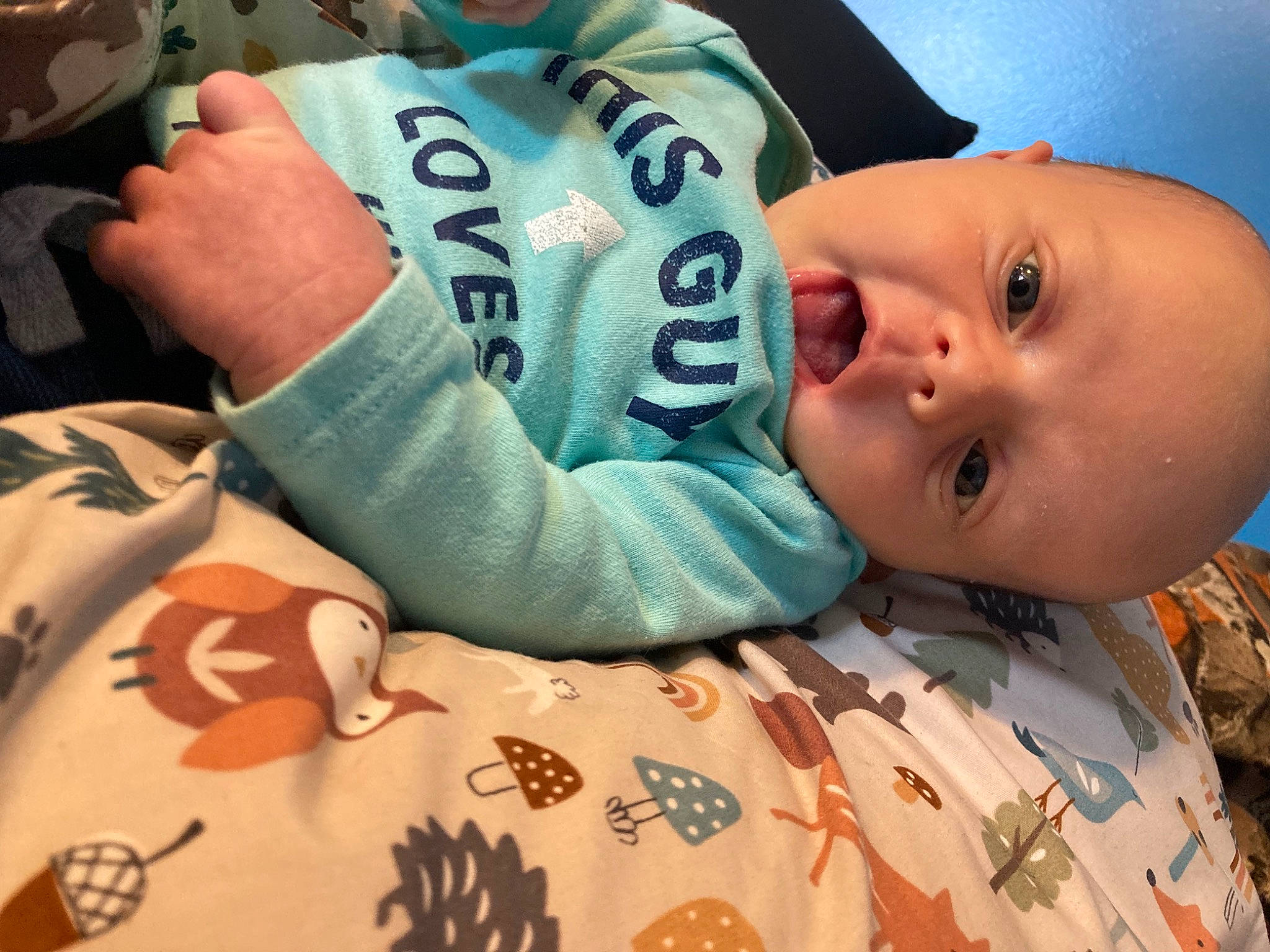 Gunner is registered to the contest to win money with this photo: arm, baby, baby_products, baby_sleeping, baby_toddler_clothing, cheek, child, comfort, finger, happy, linens, mouth, neck, nose, pattern, person, room, sitting, sleeve, t_shirt