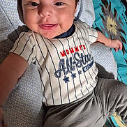 Kiran is registered to the contest to win money with this photo: baby, child, clothing, comfort, cute, fabric, face, foot, hair, hand, happy, indoors, infant, lying_down, patterned_blanket, person, portrait, smiling, striped_shirt, young_child