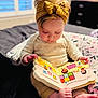 Emberlynn is registered to the contest to win money with this photo: baby, child, book, reading, headband, bed, pillow, blanket, foot, hand, indoors, clothing, toy, colorful, cute, infant, portrait, sitting, nursery, soft