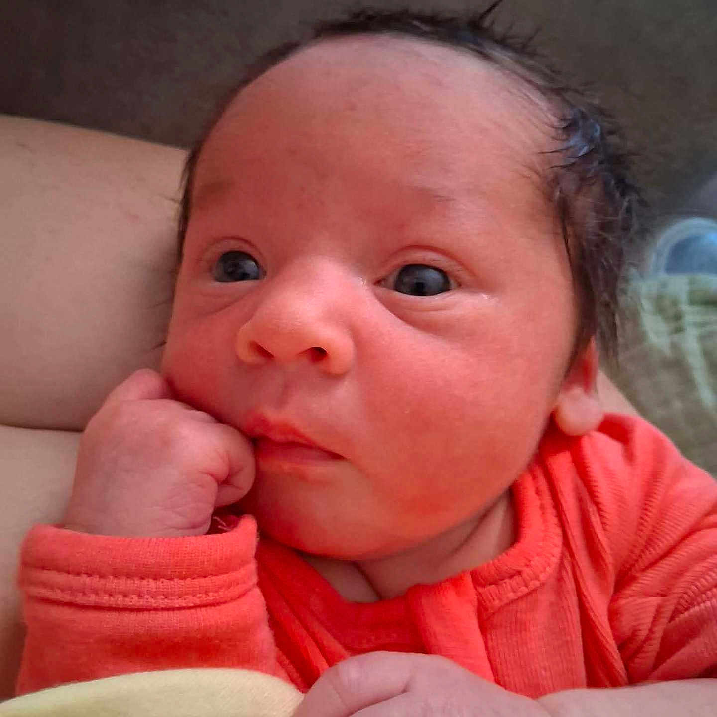 Ambria is registered to the contest to win money with this photo: baby, newborn, infant, face, hand, orange_clothing, close_up, skin, person, resting, curious, expression, indoors, soft_light, young_child, portrait, cute, small_hands, sleepy, toddler