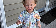 Zayden is registered to the contest to win money with this photo: toddler, child, barefoot, curly_hair, smiling, outdoor, concrete, door, shirt, shorts, patterned_clothing, happy, standing, front_portrait, house_exterior, door_mat, sidewalk, summer, cute, person
