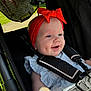 baby, child, stroller, red_bow, headband, smiling, happy, outdoor, sunlight, blanket, blue_dress, safety_harness, face, infant, cute, person, closeup, daylight, seat, cheerful