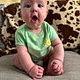 Tallulah is registered to the contest to win money with this photo: baby, child, infant, couch, blanket, cow_print, green_shirt, sun_illustration, sitting, expression, surprised, hands, feet, skin, indoors, furniture, portrait, cute, smiling_sun, person