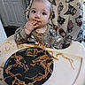 baby, high_chair, spaghetti, messy, food, plate, face, hand, blanket, hello_kitty, clothing, indoor, curious, child, feeding, tableware, kitchen, cute, mess, toddler