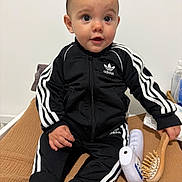 Leysson participe au concours pour gagner de l'argent avec cette photo : adidas, baby, black_clothing, blanket, bottle, child, clothing, curious, face, footwear, furniture, hairbrush, head, indoor, person, room, sitting, socks, tracksuit, young_child