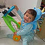 toddler, child, toy_walker, floor, smiling, blue_outfit, backpack, indoor, playful, happy, baby, colorful_toy, tile_floor, person, cute, young_child, light_blue, sitting, playtime, home