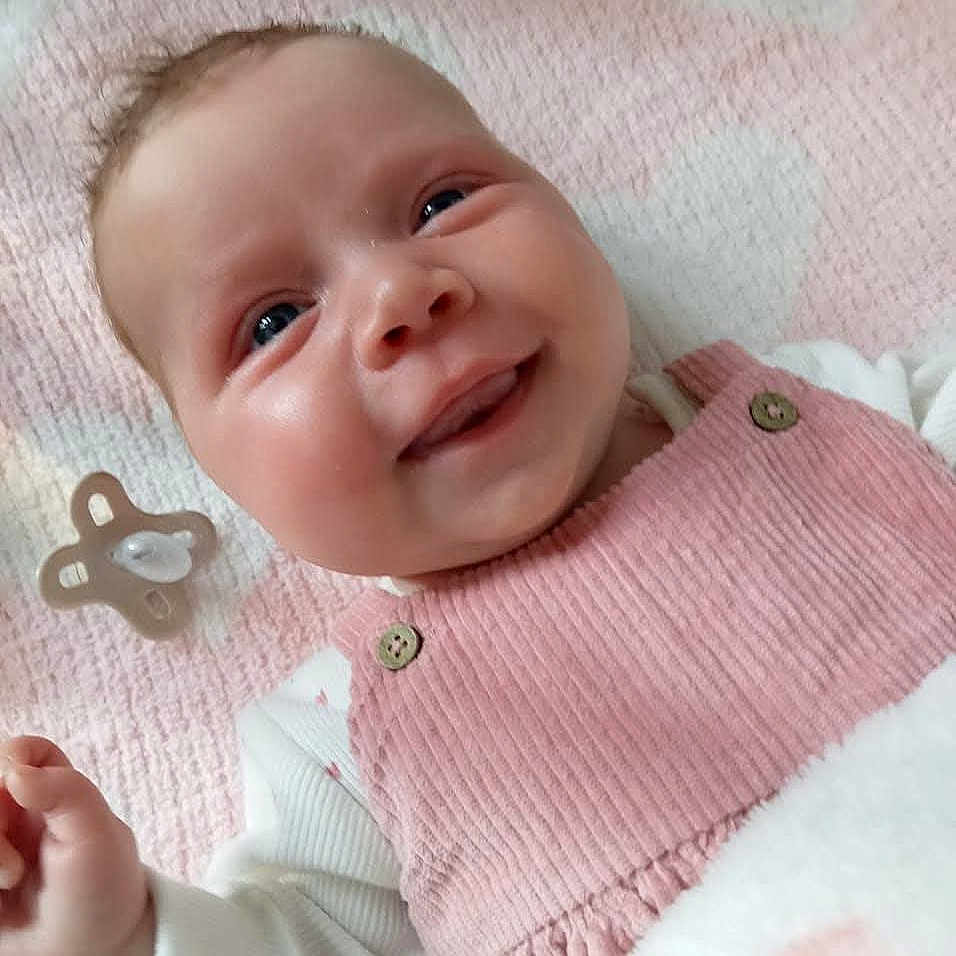 Emmi-Lei is registered to the contest to win money with this photo: baby, babywear, blanket, button, child, closeup, clothing, corduroy, cute, face, hand, happy, infant, lying_down, pacifier, pink, portrait, skin, smiling, soft