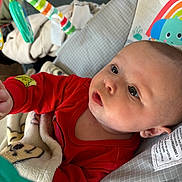 Kelsey is registered to the contest to win money with this photo: baby, infant, red_clothing, blanket, baby_seat, toy, colorful_toy, elephant_pattern, rainbow_pattern, curious, indoors, child, face, portrait, soft_texture, couch, closeup, focus, cute, young_child