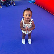 Journey is registered to the contest to win money with this photo: toddler, child, smile, clapping, blue_floor, stroller, fence, inflatable, play_area, sneakers, summer_clothing, outdoor, person, happy, playground, young_child, bright_colors, casual, fun, daylight