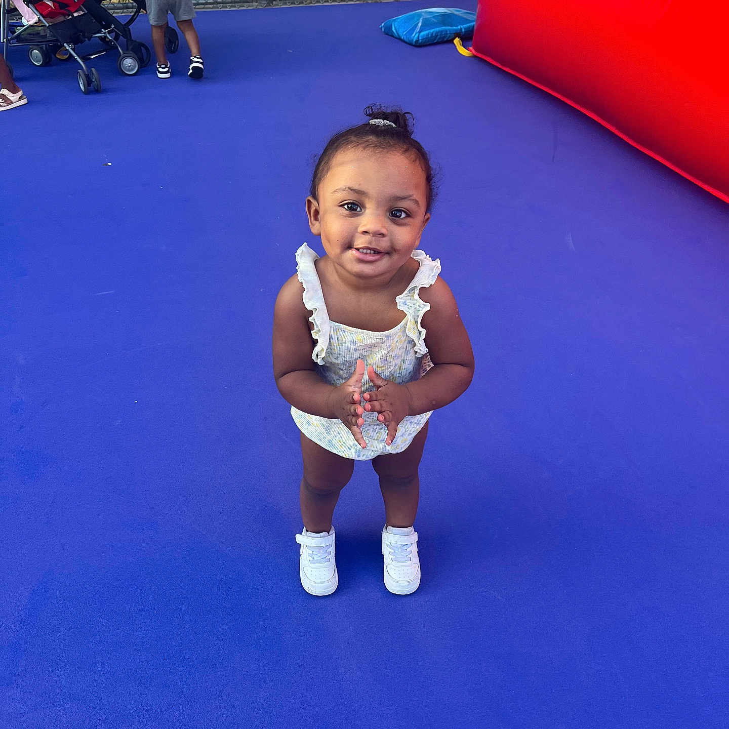 Journey is registered to the contest to win money with this photo: toddler, child, smile, clapping, blue_floor, stroller, fence, inflatable, play_area, sneakers, summer_clothing, outdoor, person, happy, playground, young_child, bright_colors, casual, fun, daylight