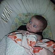 Destiny is registered to the contest to win money with this photo: baby, baby_seat, blanket, child, clothing, cushion, cute, expression, face, indoors, infant, looking_away, person, portrait, resting, sleeping_area, soft_lighting, wide_eyes, wrapped, young_child