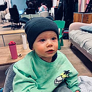 Charly a rejoint le concours — aidez-le/la à gagner de superbes lots ! toddler, child, indoor, hat, bear_ears, green_sweater, toy, wooden_toy, face, blue_eyes, person, sitting, couch, chair, people, computer, room, floor, clothing, casual