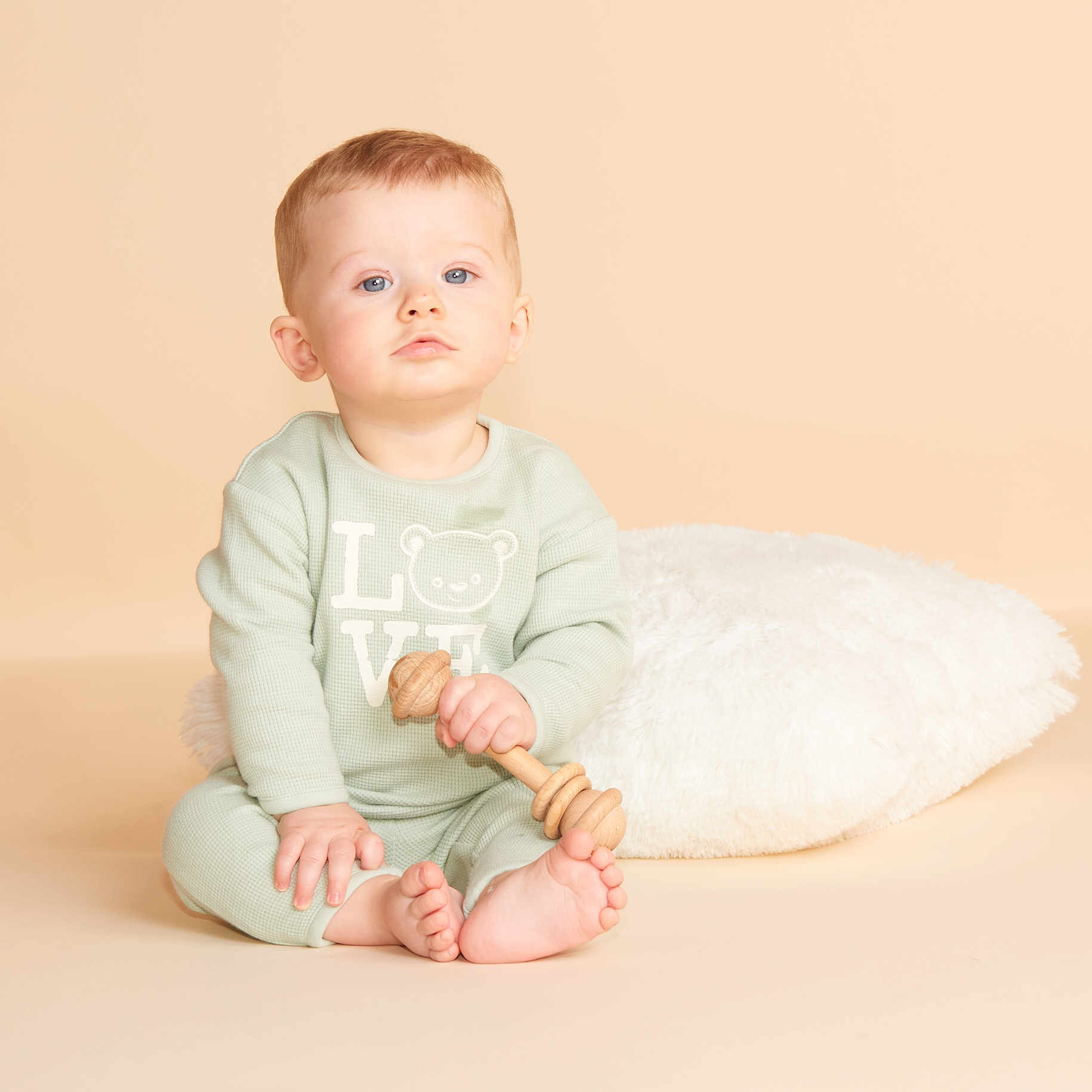 Charly participe au concours pour gagner de l'argent avec cette photo : baby, child, infant, pajamas, wooden_toy, rattle, floor, pillow, indoor, portrait, sitting, cute, serious, minimalist, soft_light, beige_background, feet, hands, face, person