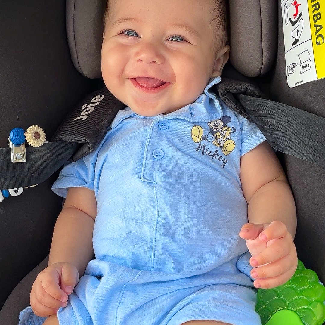 Swann a rejoint le concours — aidez-le/la à gagner de superbes lots ! baby, blue_clothing, car_seat, child, closeup, cute, face, happy, head, indoor, infant, mickey_mouse, person, romper, seatbelt, sitting, skin, smiling, teething_toy, toy