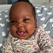 Amrryn Williams is registered to the contest to win money with this photo: baby, smiling, face, tongue_out, floral_clothing, pillow, heart_pattern, cute, infant, closeup, happy, child, portrait, indoors, skin, head, expression, person, warm, cozy