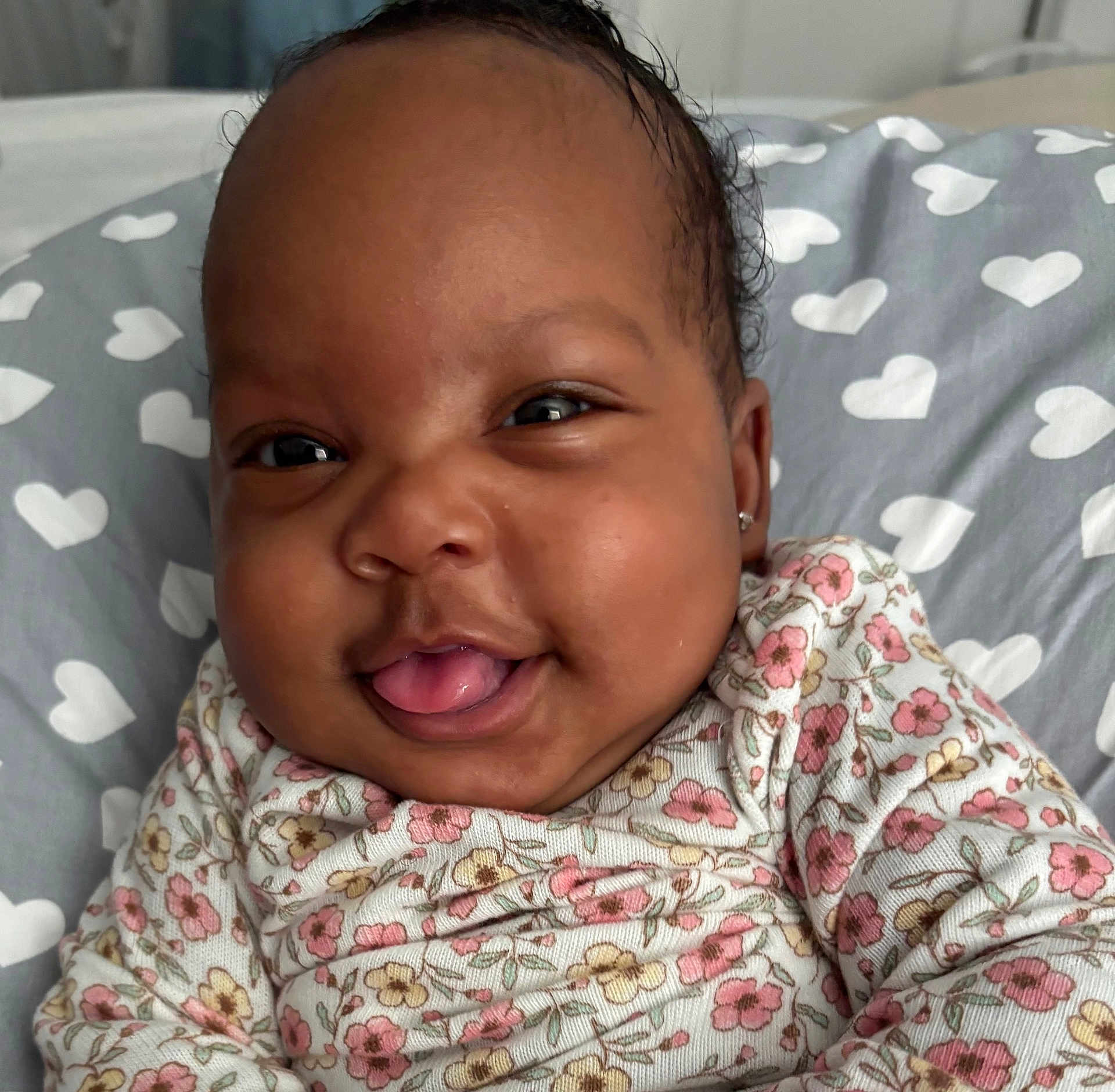 Amrryn Williams is registered to the contest to win money with this photo: baby, smiling, face, tongue_out, floral_clothing, pillow, heart_pattern, cute, infant, closeup, happy, child, portrait, indoors, skin, head, expression, person, warm, cozy