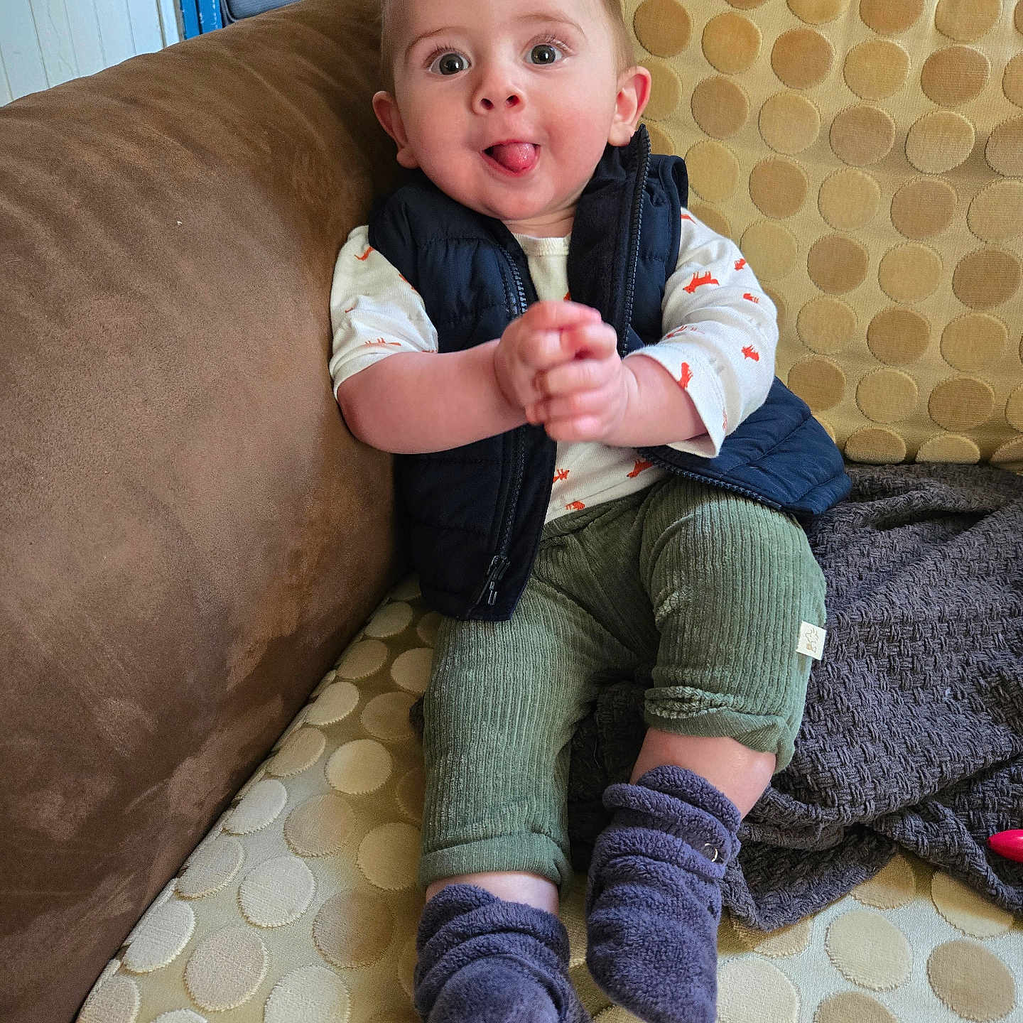 Jordan joined the competition — help win amazing prizes! baby, child, couch, clothing, vest, pants, socks, tongue, hands, face, indoor, pattern, furniture, playful, smile, person, sitting, expression, cute, home