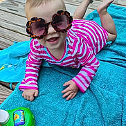 Serene joined the competition — help win amazing prizes! baby, sunglasses, striped_clothing, pink, blue_towel, wooden_deck, toy, happy, smiling, child, outdoor, playtime, colorful, infant, cute, summer, fun, lying_down, hand, feet