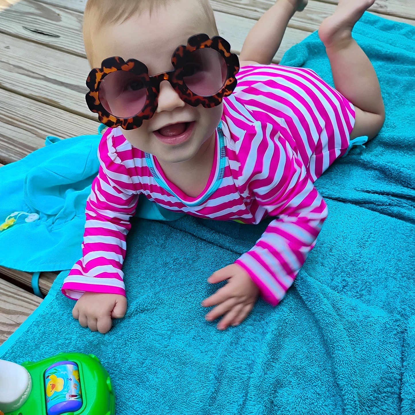 Serene joined the competition — help win amazing prizes! baby, blue_towel, child, colorful, cute, feet, fun, hand, happy, infant, lying_down, outdoor, pink, playtime, smiling, striped_clothing, summer, sunglasses, toy, wooden_deck