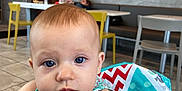 Serene joined the competition — help win amazing prizes! baby, background_person, blue_eyes, casual_dining, chair, child, clothing, colorful_blanket, curious_expression, face, floor_tiles, high_chair, indoor, infant, light, patterned_fabric, person, portrait, reaching_hand, table