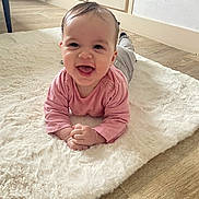 Salomé participe au concours pour gagner de l'argent avec cette photo : baby, cabinet, child, cute, face, flooring, fluffy_rug, gray_pants, hands_clasped, happy, home, indoors, lying_down, natural_light, pink_shirt, portrait, smiling, white_rug, wooden_floor, young_child