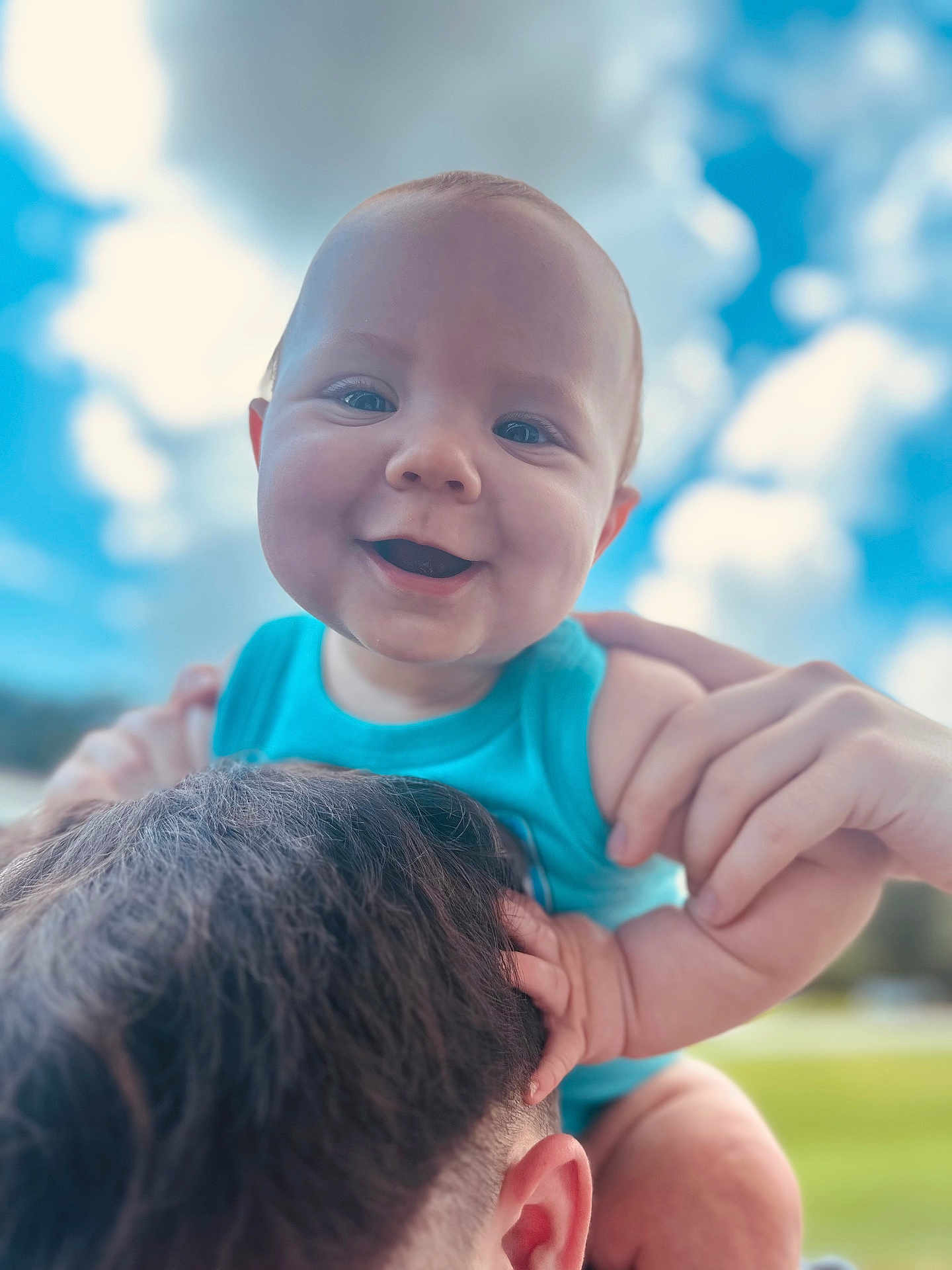 Cooper is registered to the contest to win money with this photo: baby, child, smiling, blue_sky, clouds, outdoor, person, shoulders, happy, face, hands, short_hair, holding, young_child, sunlight, nature, portrait, skin, joy, casual_clothing