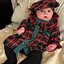 Elda-Rose is registered to the contest to win money with this photo: baby, bed, black_tights, blanket, buttoned_shirt, child, clothing, cozy, cute, expression, fabric, hat, headwear, indoors, infant, person, plaid_clothing, portrait, sitting, young_child