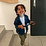 child, boy, smiling, curly_hair, denim_jacket, white_shirt, green_pants, sneakers, indoor, tiles, stairs, door, keys, happy, playing, person, holding, young, casual_clothing, home