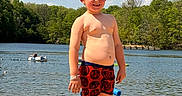 James is registered to the contest to win money with this photo: child, boy, beach, lake, water, sand, swim_shorts, sunny, outdoor, nature, trees, person, floating, inner_tube, summer, barefoot, sky, clouds, recreation, daytime
