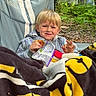 James is registered to the contest to win money with this photo: child, boy, blanket, camping_chair, cookie, snack, forest, outdoor, tent, trees, leaves, nature, smiling, blond_hair, casual_clothing, relaxation, daylight, recreation, happy, portrait
