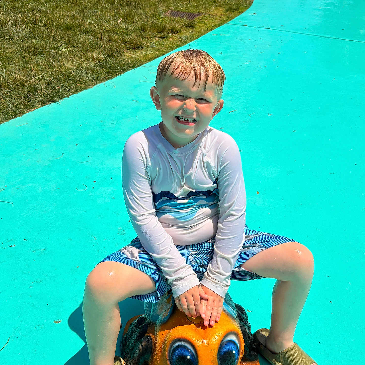 James joined the competition — help win amazing prizes! child, boy, swimwear, splash_pad, frog_statue, outdoor, summer, grass, water_play_area, playground, happy, smiling, sunny_day, feet, sandals, shorts, long_sleeve_shirt, toy, recreation, fun