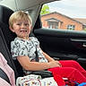 James is registered to the contest to win money with this photo: child, boy, car_interior, car_seat, seatbelt, blonde_hair, smiling, red_pants, graphic_tshirt, mickey_mouse, bag, blanket, window, house, daylight, sitting, casual_clothing, happy, road_trip, passenger