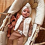baby, bassinet, child, cozy, cushion, cute, headwear, indoor, infant, knitwear, portrait, sleeping_area, smiling, socks, stuffed_animal, toy, vest, wicker, wooden_floor, wooden_sign