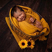 Tanush joined the competition — help win amazing prizes! baby, infant, newborn, wrapped, yellow, blanket, basket, wooden_floor, sunflowers, smiling, winking, cute, cozy, portrait, child, feet, hand, knitwear, indoor, warm_colors