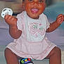 baby, child, smiling, pacifier, bows, hair_accessories, pink_clothing, bib, toy_phone, sitting, happy, indoors, cute, infant, playful, portrait, sparkles, dark_skin, short_hair, cheerful