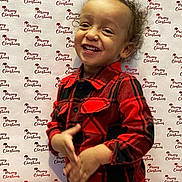 Khalil joined the competition — help win amazing prizes! toddler, child, smiling, curly_hair, plaid_shirt, red_clothing, black_clothing, holiday, christmas, background, festive, portrait, indoors, happy, cute, person, standing, clothing, young_child, celebration